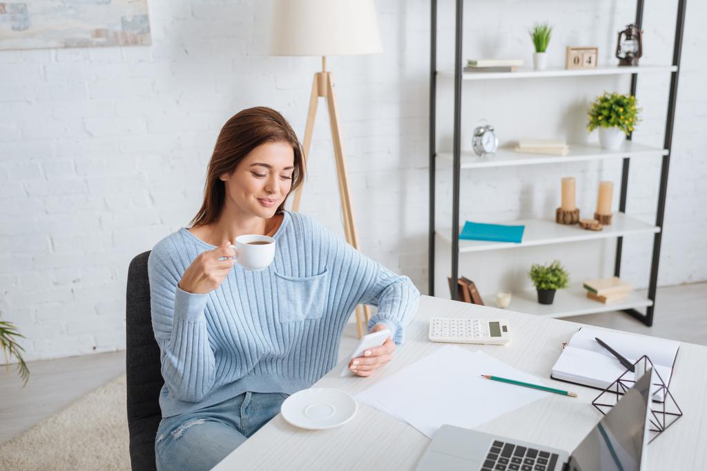 mulher feliz usando smartphone enquanto segurando xícara de café e refrigeração em casa
  - Foto, Imagem