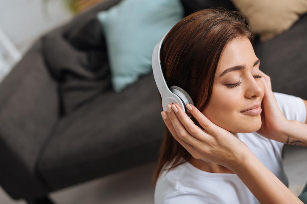 álmodozó lány hallgat zenét fülhallgató közelében kanapé  - Fotó, kép