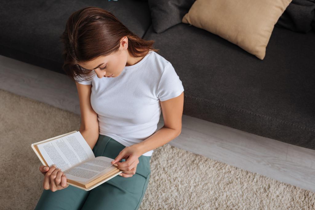 vista aerea di ragazza lettura libro mentre seduto sul tappeto vicino divano
  - Foto, immagini