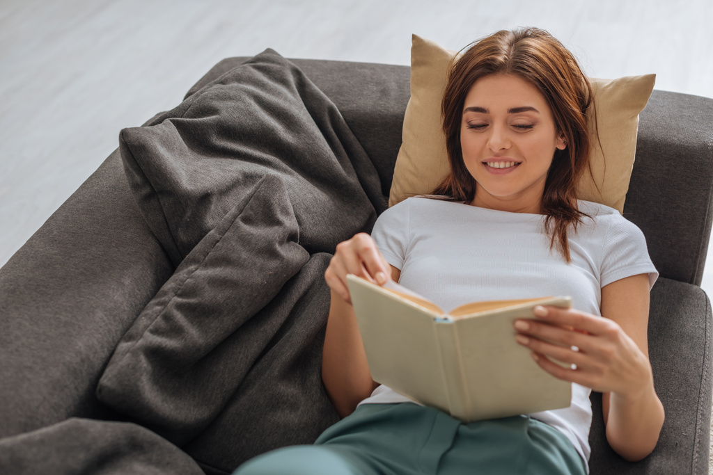 allegra giovane donna che legge libro mentre si rilassa sul divano in soggiorno
  - Foto, immagini