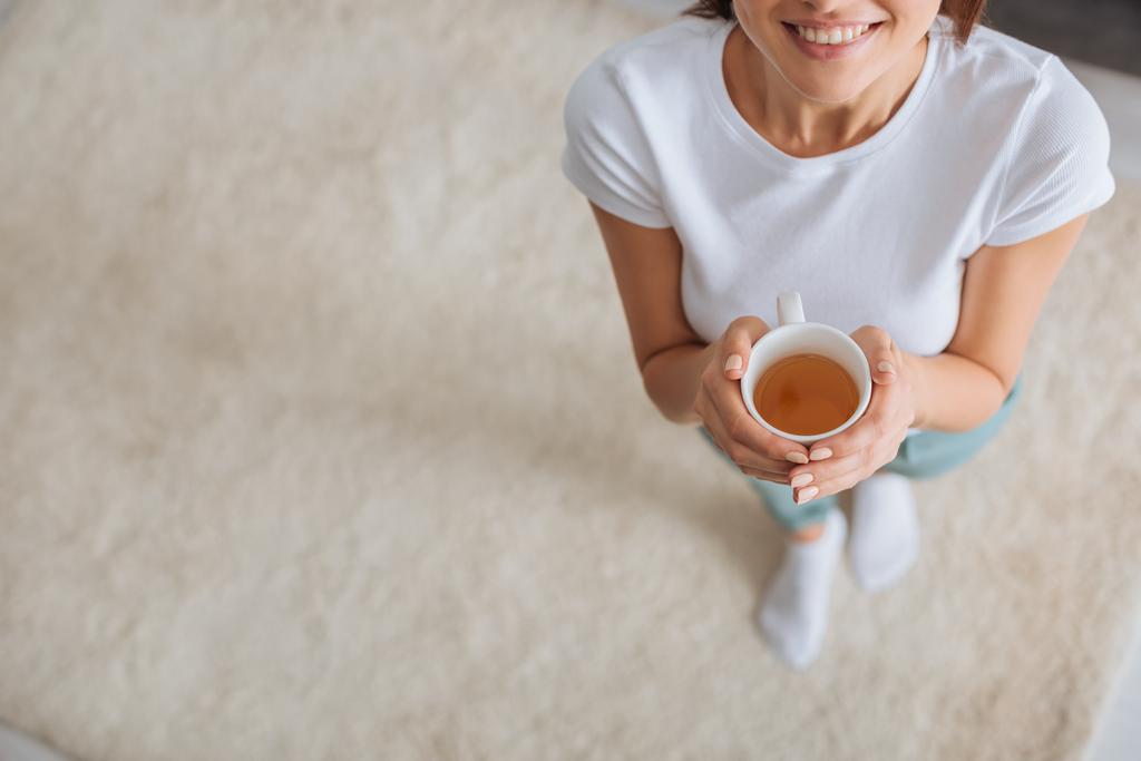 abgeschnittene Ansicht eines glücklichen Mädchens mit Tasse und Tee  - Foto, Bild