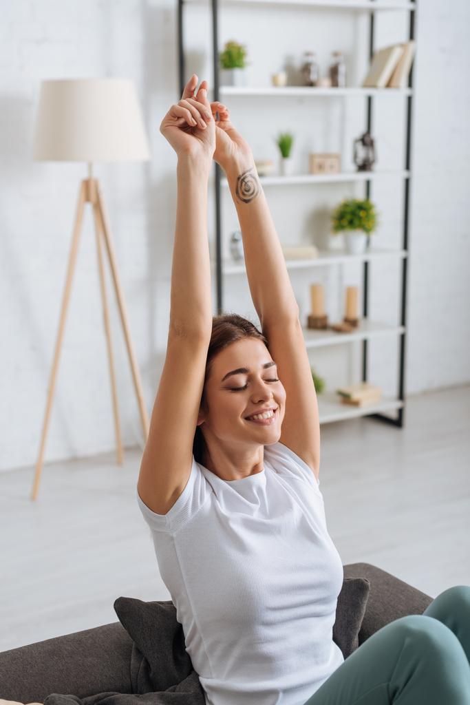 getatoeëerde vrouw met uitgestrekte handen glimlachend en ontspannen in de woonkamer  - Foto, afbeelding