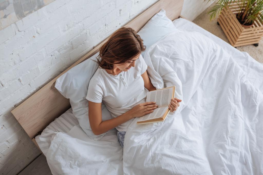 вид зверху щаслива жінка читає книгу під час холоду в ліжку
  - Фото, зображення