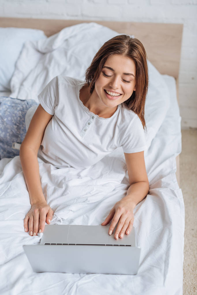 boldog lány használja laptop, miközben hűtés a hálószobában  - Fotó, kép