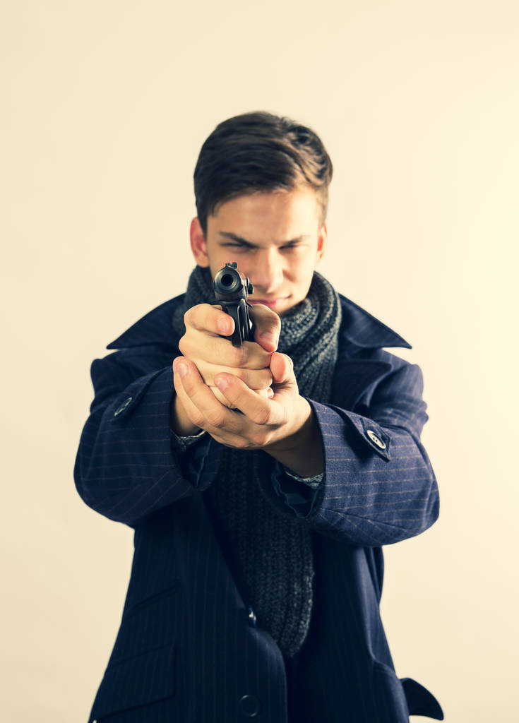 Jongeman crimineel mikt met pistool op lichte achtergrond. Selectieve focus. - Foto, afbeelding