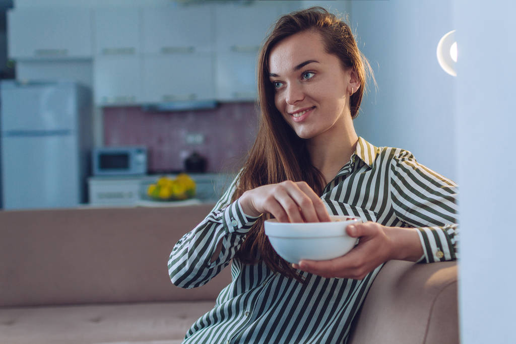 Retrato de jovem mulher atraente comendo pipoca e assistindo tv em casa sozinho
  - Foto, Imagem