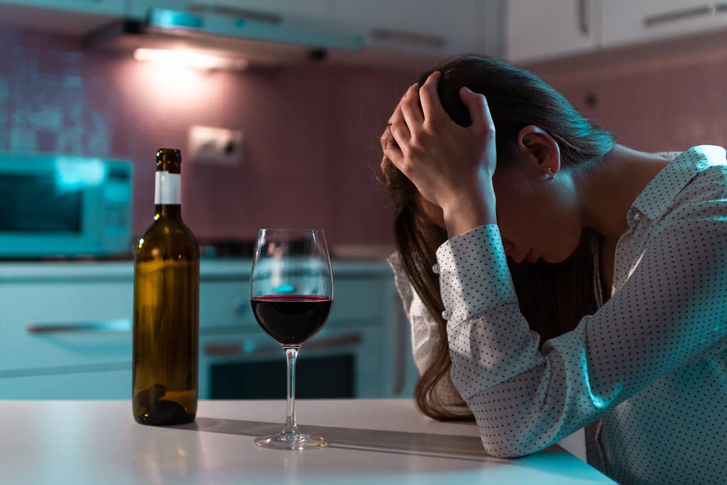 Mutsuz, yalnız, kırmızı şaraplı genç bir kadın akşamları evde tek başına içiyor. Hayat zorlukları ve sorunlar. Kadın alkolizmi ve alkol bağımlılığı - Fotoğraf, Görsel