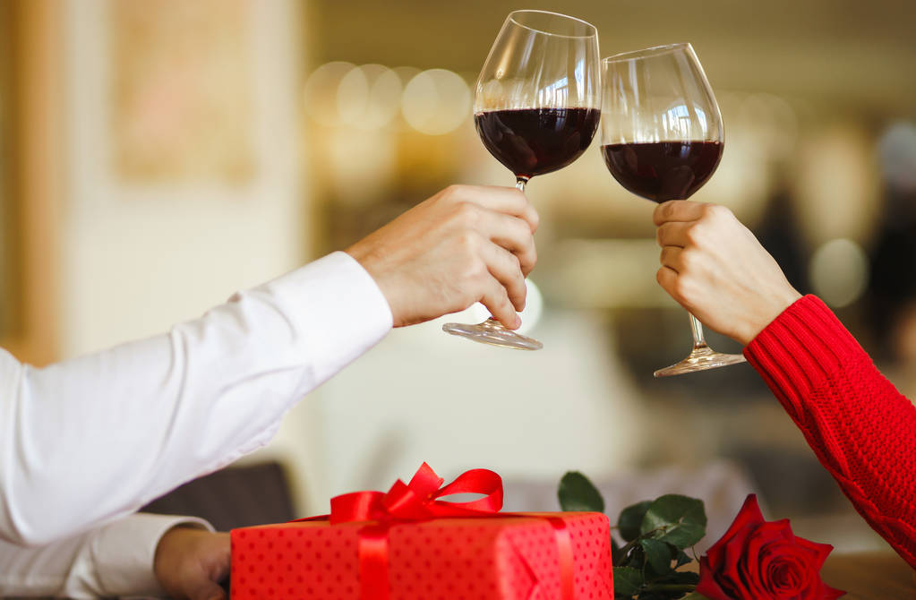 Руки, держащие бокалы вина на фоне ресторана. Пара стаканов с красным вином. День святого Валентина концепции празднования. Отношения, неожиданность и концепция любви
. - Фото, изображение