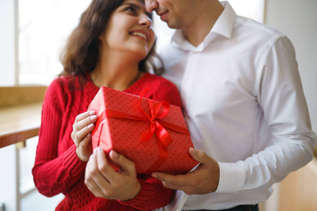 Hediye kucaklaşması olan mutlu çift. Birbirine aşık bir çiftin elinde kırmızı hediye kutusu. Sevgililer Günü, tatil ve sürpriz konsept. Sevgililer birbirlerine hediyeler verir. İlişki ve aşk kavramı. - Fotoğraf, Görsel