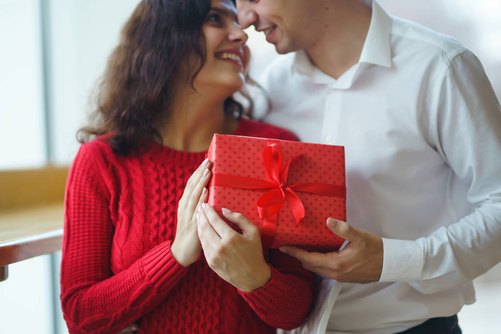 Hediye kucaklaşması olan mutlu çift. Birbirine aşık bir çiftin elinde kırmızı hediye kutusu. Sevgililer Günü, tatil ve sürpriz konsept. Sevgililer birbirlerine hediyeler verir. İlişki ve aşk kavramı. - Fotoğraf, Görsel
