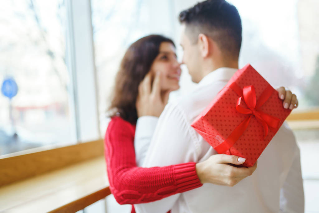 ギフトの抱擁で幸せなカップル。愛のカップルの手の中に赤いギフトボックス。バレンタインデー、休日や驚きのコンセプト。恋人同士でプレゼントする。関係と愛の概念. - 写真・画像