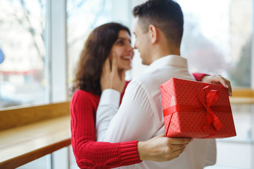 Szczęśliwa para z uściskiem prezentów. Czerwone pudełko w rękach zakochanej pary. Walentynki, wakacje i pomysł na niespodziankę. Kochankowie dają sobie prezenty. Związek i koncepcja miłości. - Zdjęcie, obraz