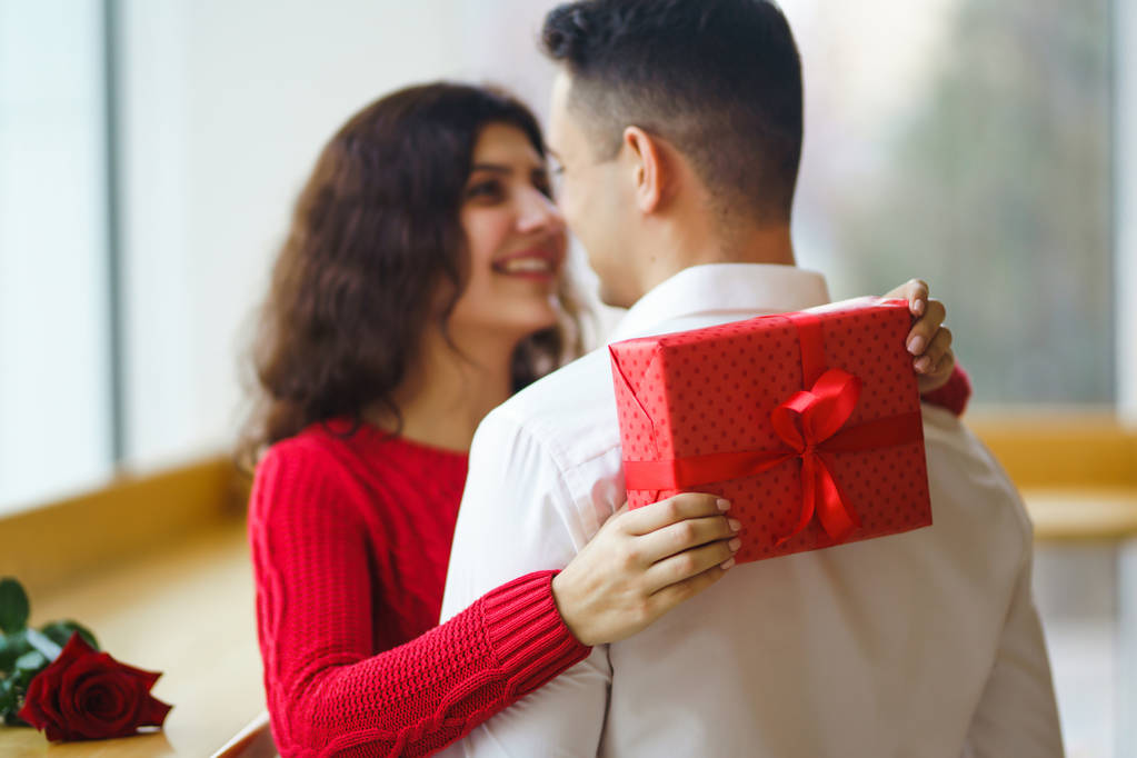 Boldog pár, ajándéköleléssel. Piros ajándékdoboz egy szerelmes pár kezében. Valentin-nap, ünnep és meglepetés koncepció. A szerelmesek ajándékot adnak egymásnak. Kapcsolat és szerelem fogalma. - Fotó, kép