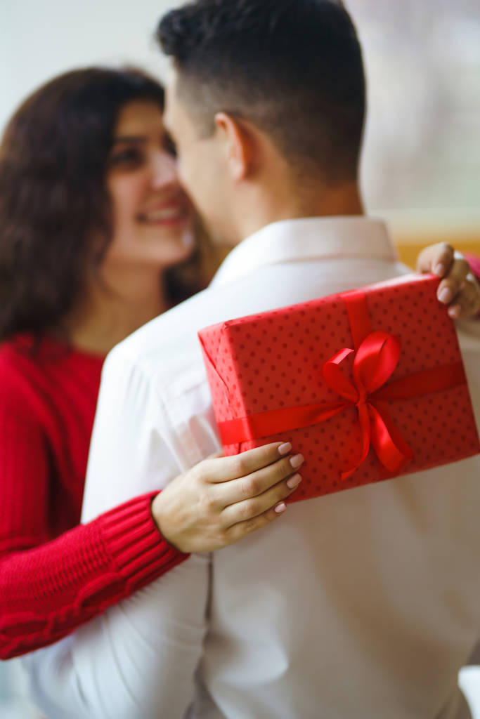 Szczęśliwa para z uściskiem prezentów. Czerwone pudełko w rękach zakochanej pary. Walentynki, wakacje i pomysł na niespodziankę. Kochankowie dają sobie prezenty. Związek i koncepcja miłości. - Zdjęcie, obraz