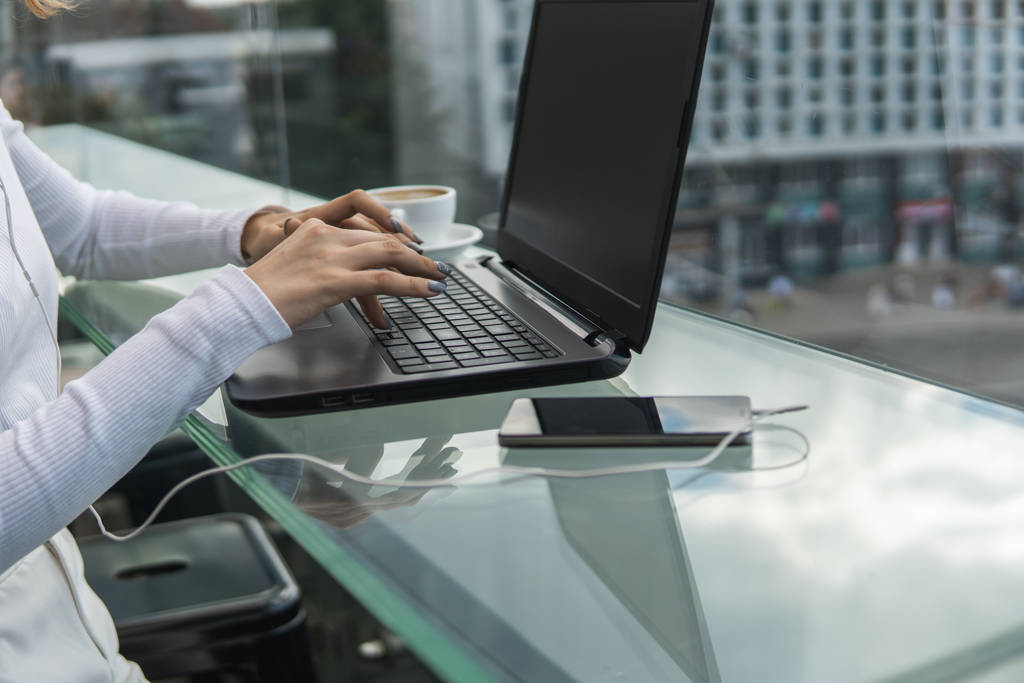 Жінка працює за допомогою портативного комп'ютера на столі. Руки, які друкуються на клавіатурі. Жінка-підприємець друкує на клавіатурі ноутбука, сидячи в кафе
. - Фото, зображення