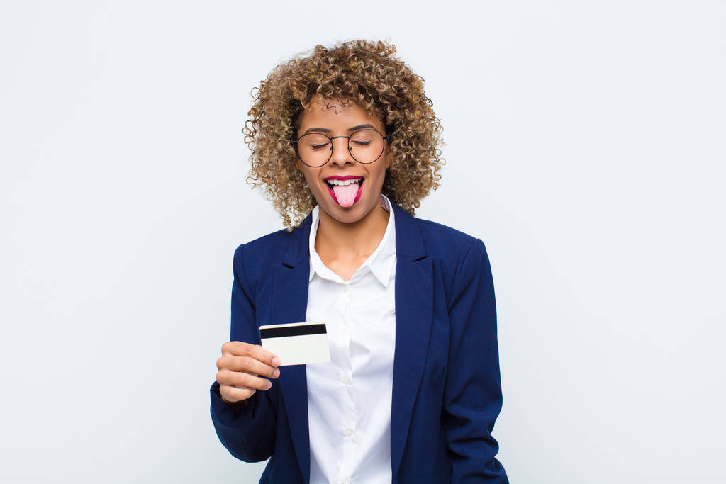 mladá africká Američanka s veselým, bezstarostným, vzpurným postojem, vtipem a vystrčeným jazykem, baví se s kreditní kartou - Fotografie, Obrázek