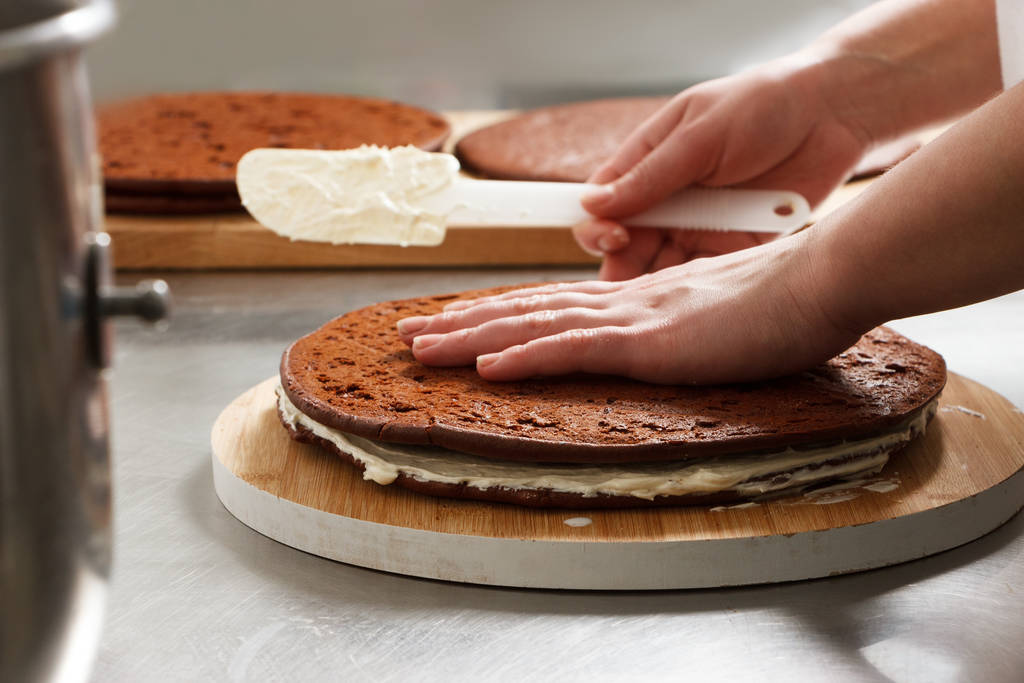 Frau bereitet Schokoladenkuchen mit Milchcreme zu. der Prozess der Herstellung des Schokoladenkuchens, vom Anfang bis zum Ende. Handarbeit für Süßwaren. - Foto, Bild
