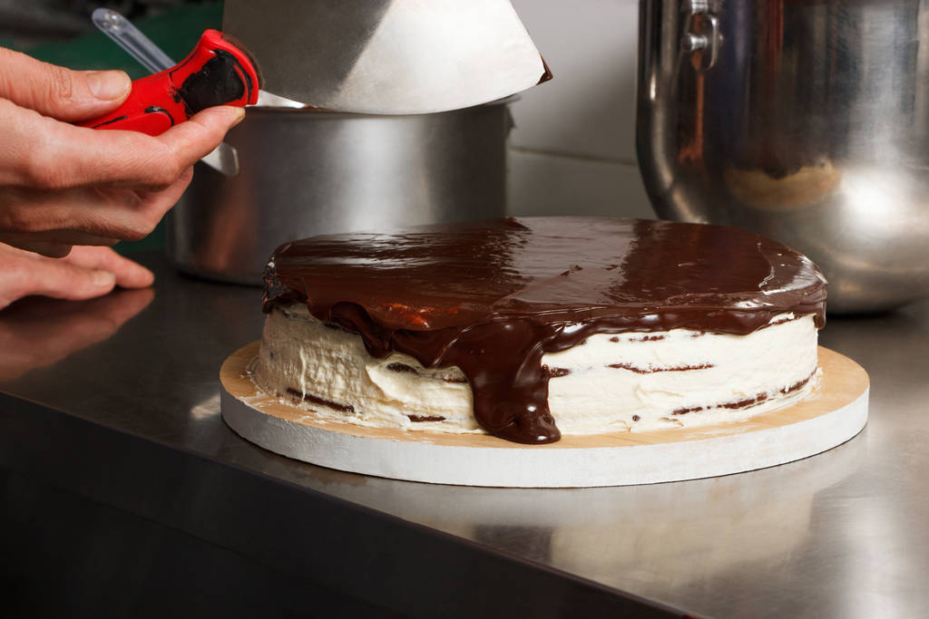 Nainen tahraa suklaakakku lasite kuorrutus, loppuvaiheessa ruoanlaitto. Suklaakakun valmistusprosessi alusta loppuun. Valmistettu käsin makeisia varten
. - Valokuva, kuva