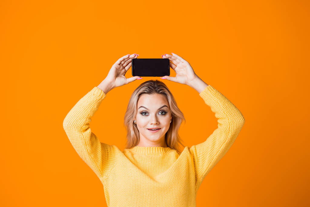 Мила молода жінка в жовтому светрі тримає смартфон
 - Фото, зображення