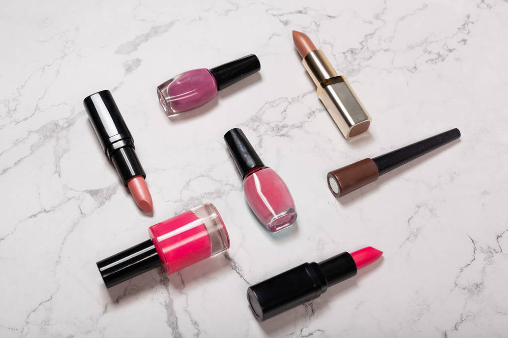 Cosmetic products on marble texture. Lipsticks, nail varnish, makeup brushes on white marble background - 写真・画像