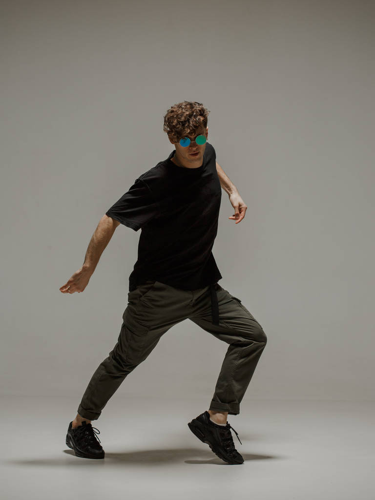 Ένας τύπος που χορεύει σύγχρονο χορό στο στούντιο. Ουδέτερο γκρι φόντο. Ακροβάτης χορευτής bboy. - Φωτογραφία, εικόνα