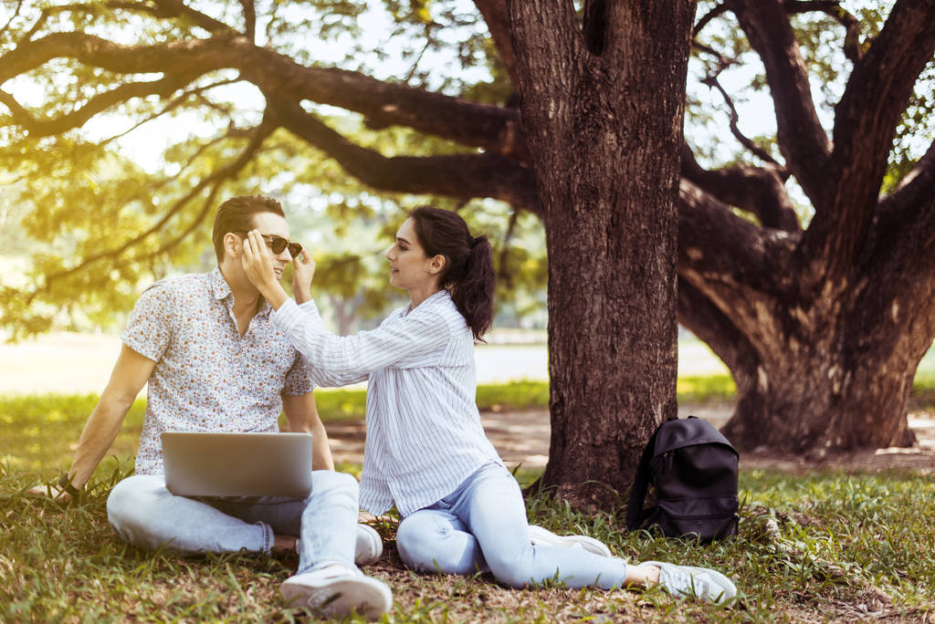 Genç çiftler parkta birlikte oturup oynuyorlar, romantik ve mutlu anların tadını çıkarıyorlar, mutlu ve gülümsüyorlar. - Fotoğraf, Görsel