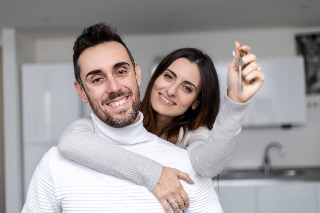 Onnellinen pari halaamassa uudessa kodissaan, nainen näyttämässä uusia avaimia - Valokuva, kuva