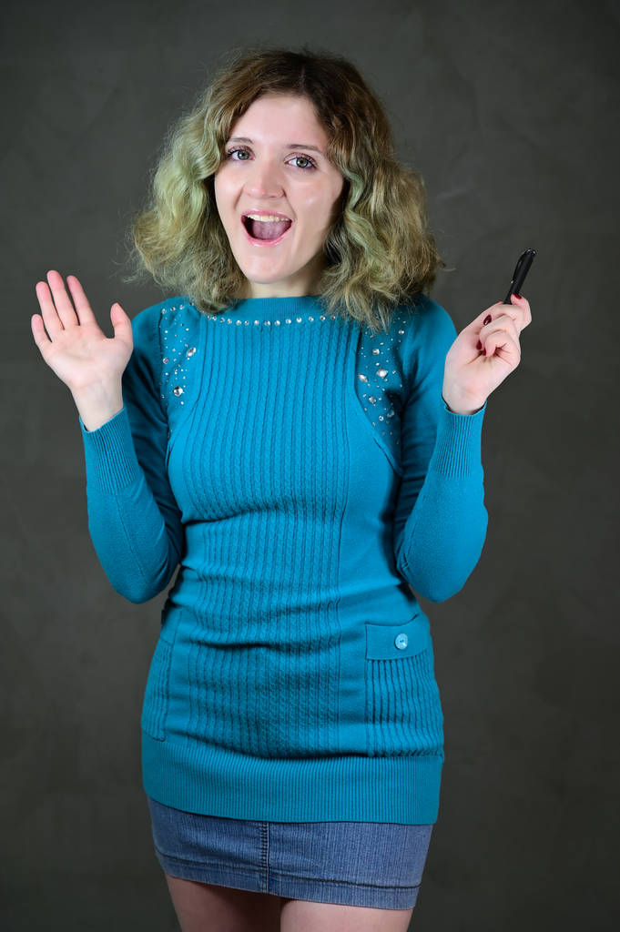 Concepto de foto vertical de una mujer joven con emociones en un vestido azul. Retrato de una bonita estudiante con hermoso pelo rizado está de pie delante de la cámara sobre un fondo gris
. - Foto, imagen
