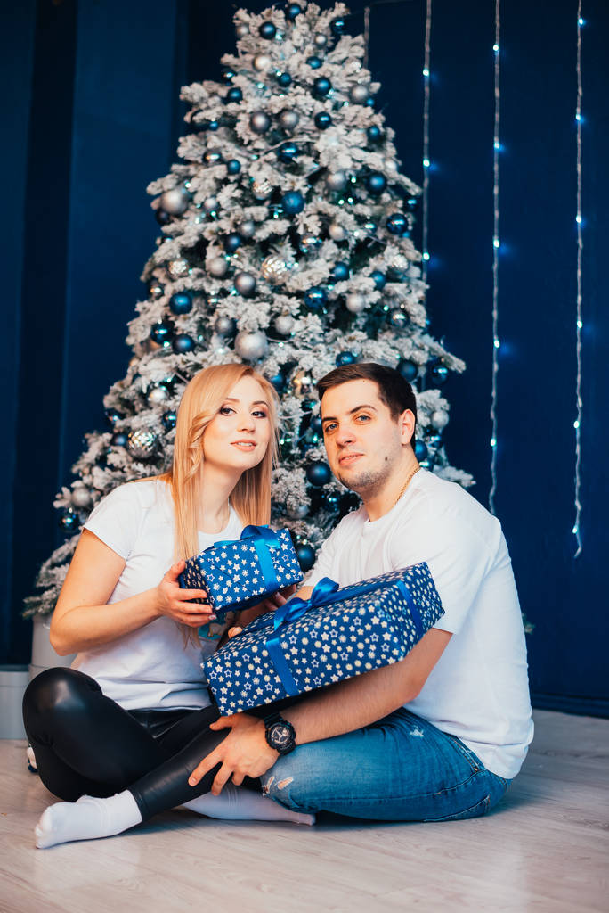 счастливая молодая пара с подарками, сидя вместе возле рождественской елки
 - Фото, изображение