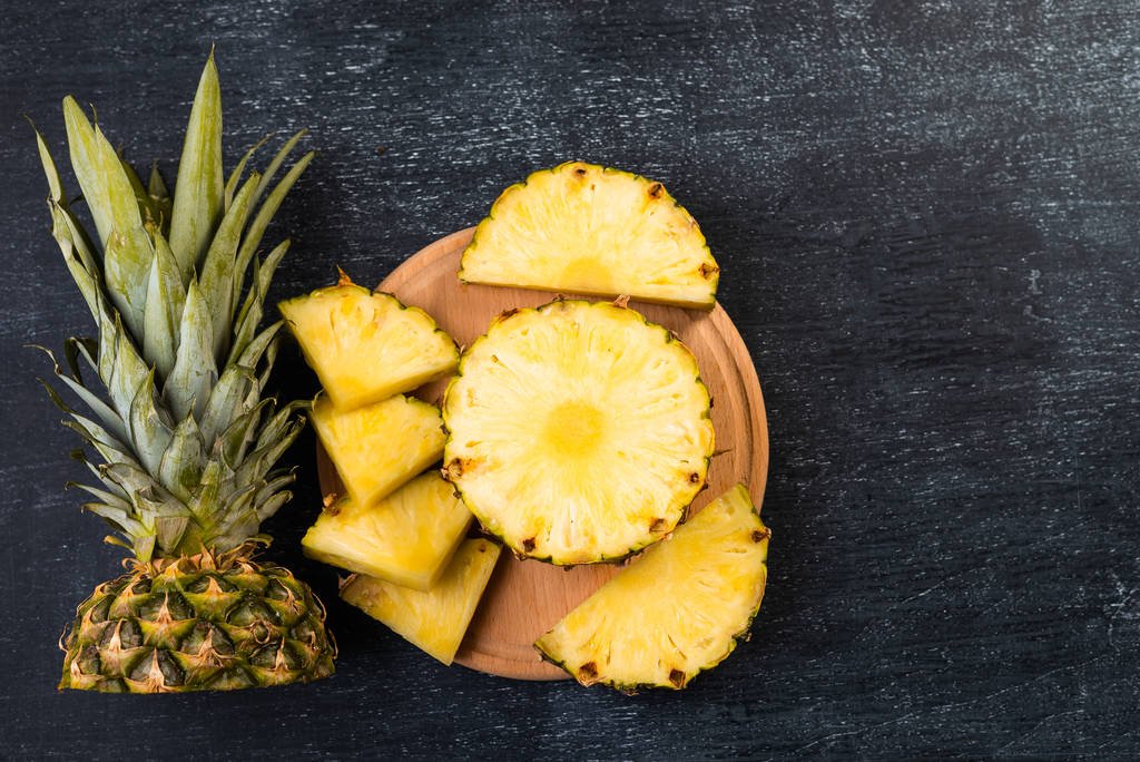 Draufsicht auf frisch geschnittene Ananas auf Holzbrett auf dunklem Hintergrund   - Foto, Bild