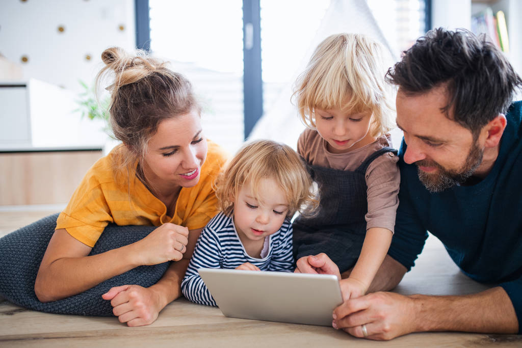 Jonge familie met twee kleine kinderen in de slaapkamer, met behulp van tablet. - Foto, afbeelding