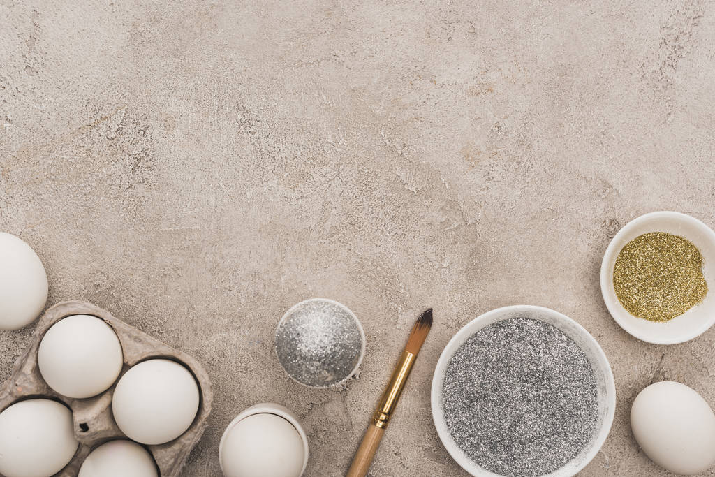 Tavuklu yumurta, gümüş ve altın parıltılı gri beton yüzeyde boya fırçaları. - Fotoğraf, Görsel