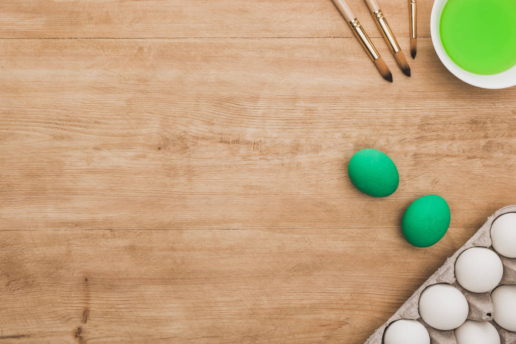вид зверху на зелену акварельну фарбу в мисці біля курячих яєць і пензлів на дерев'яному столі
 - Фото, зображення