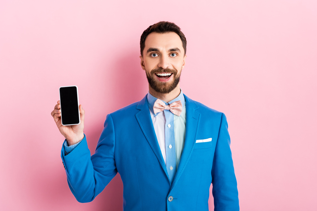 happy bearded businessman holding smartphone with blank screen on pink  - 写真・画像