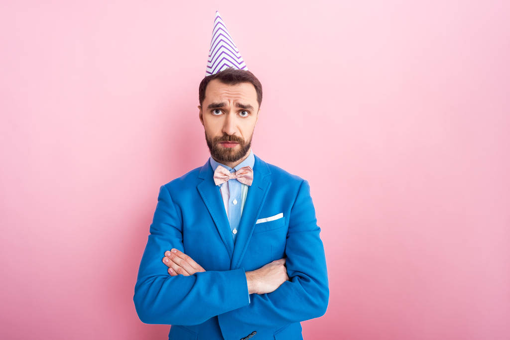 offended businessman in party cap standing with crossed arms on pink  - Photo, Image
