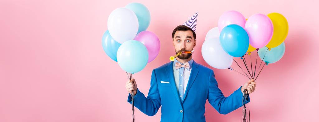 panoramisch schot van zakenman in party cap houden ballonnen op roze  - Foto, afbeelding