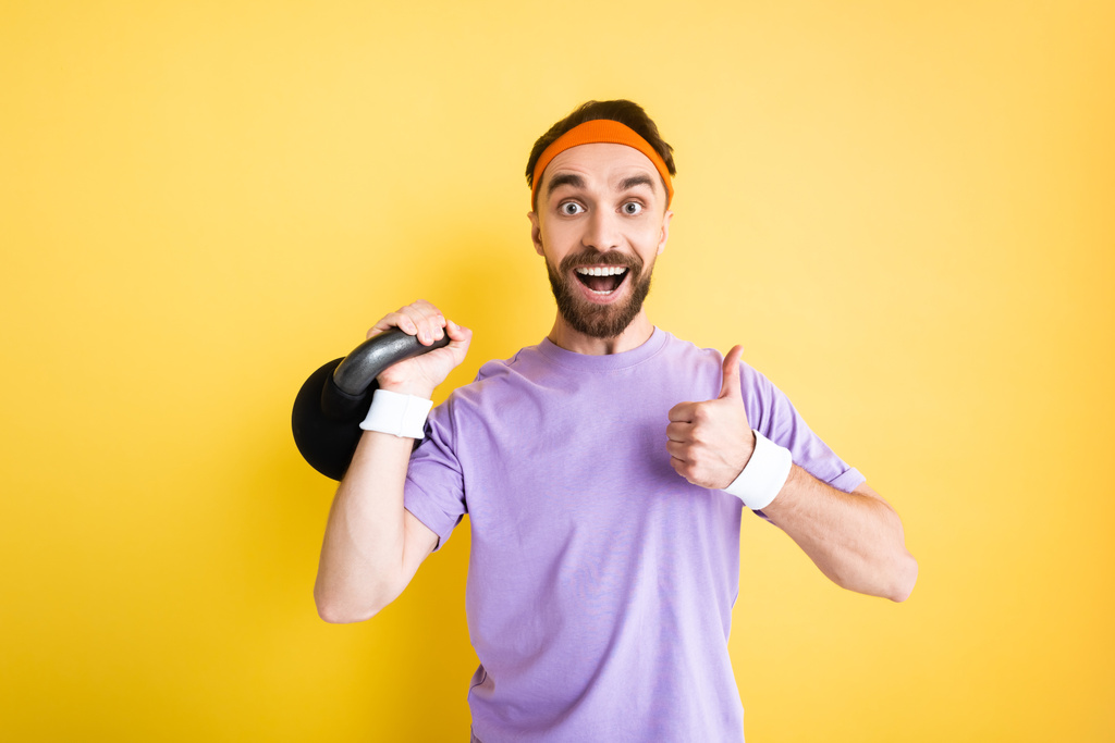 fröhlicher Sportler mit schwerer Hantel und erhobenem Daumen vereinzelt auf gelb - Foto, Bild