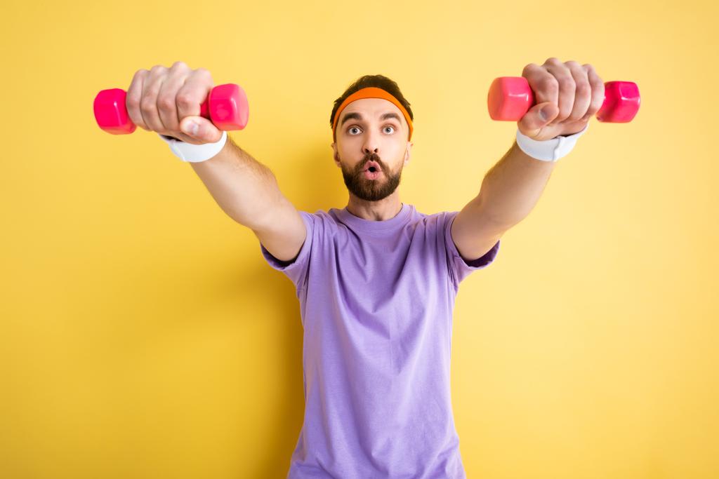 Selektiver Fokus des bärtigen Sportlers beim Training mit kleinen rosa Hanteln auf gelb - Foto, Bild
