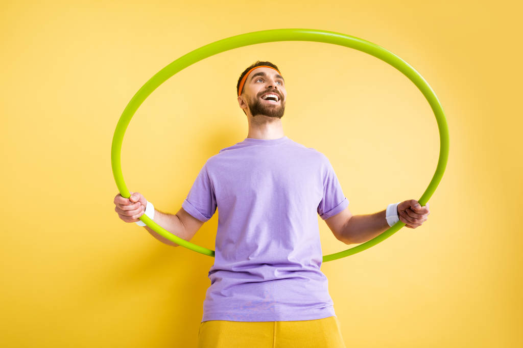 vista de ángulo bajo de deportista alegre ejercitando con hula hoop en amarillo
 - Foto, imagen