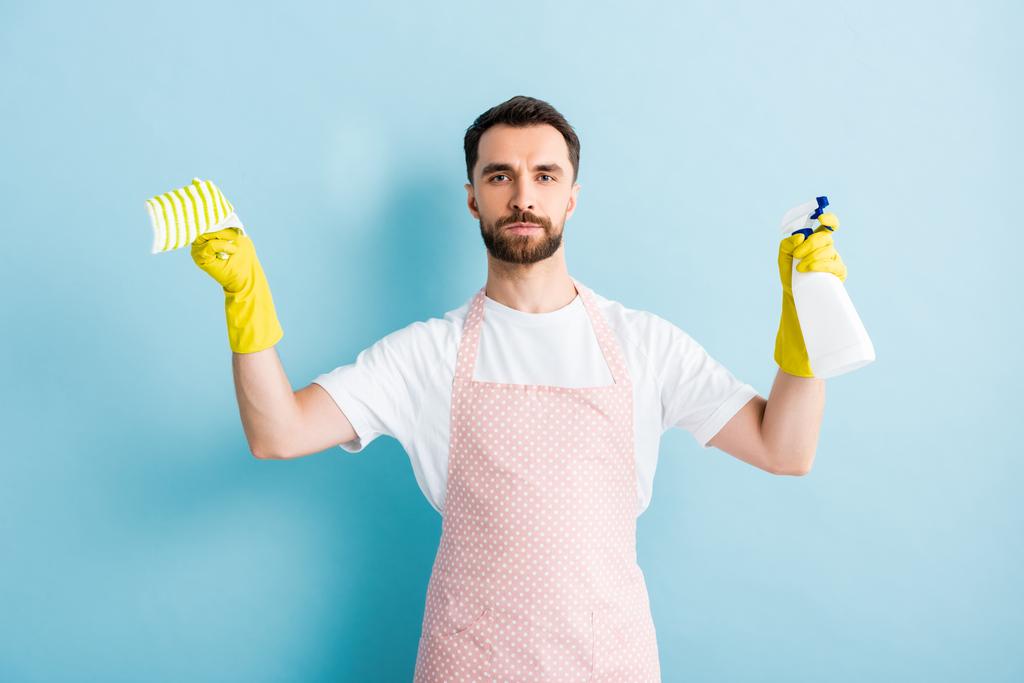 бородатий чоловік тримає ганчірку і пляшку спрею для прибирання на синьому
   - Фото, зображення