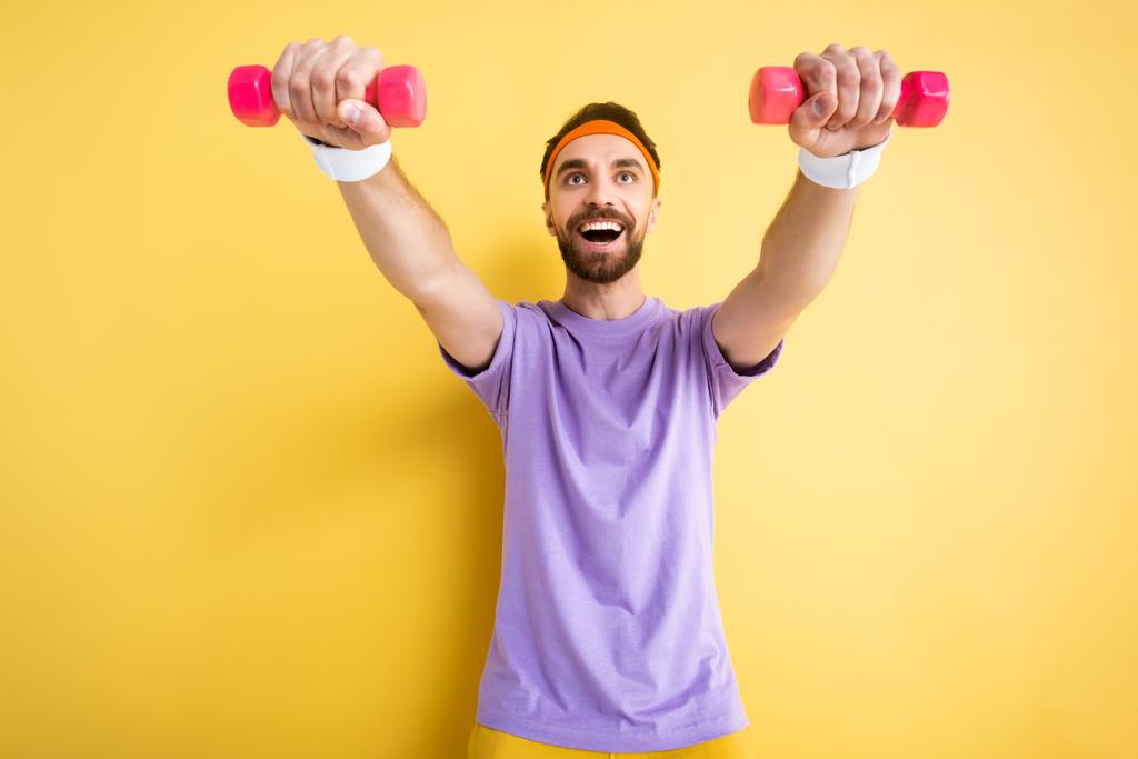 Tiefansicht des aufgeregten Sportlers beim Training mit kleinen rosafarbenen Hanteln auf gelb - Foto, Bild