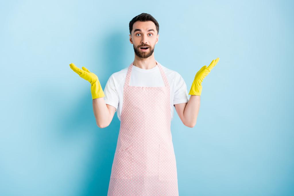 bearded man in pink dotted apron showing shrug gesture on blue  - Photo, Image