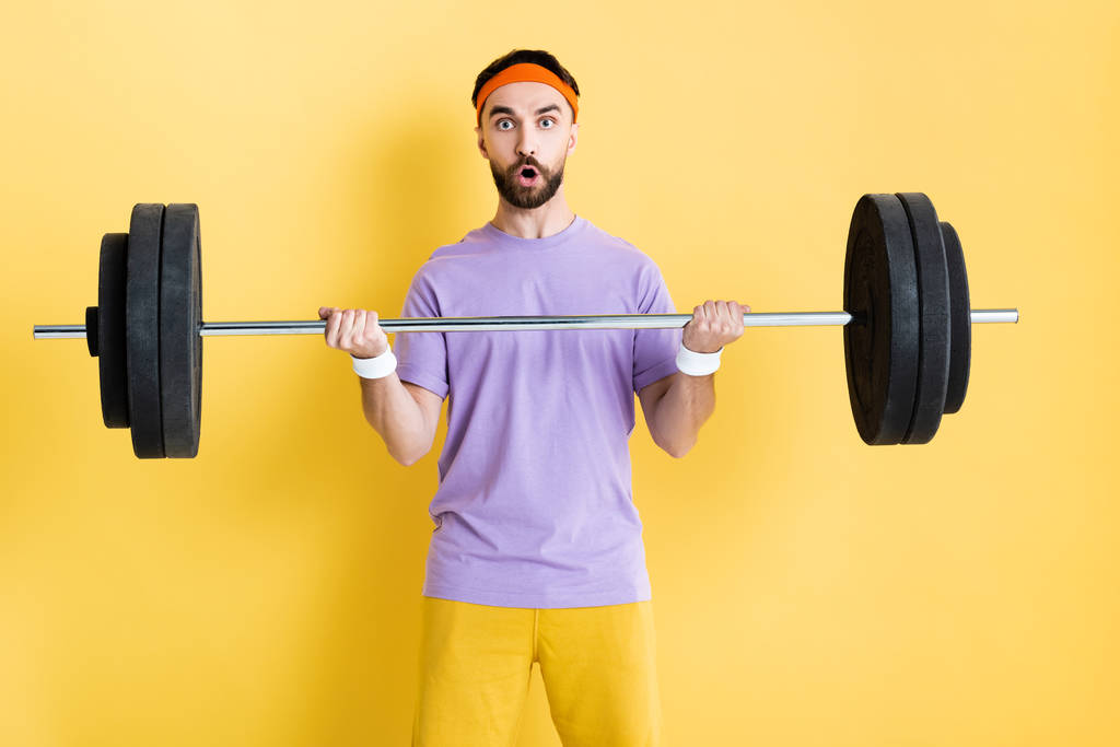 shocked sportsman working out with barbell on yellow - Photo, Image