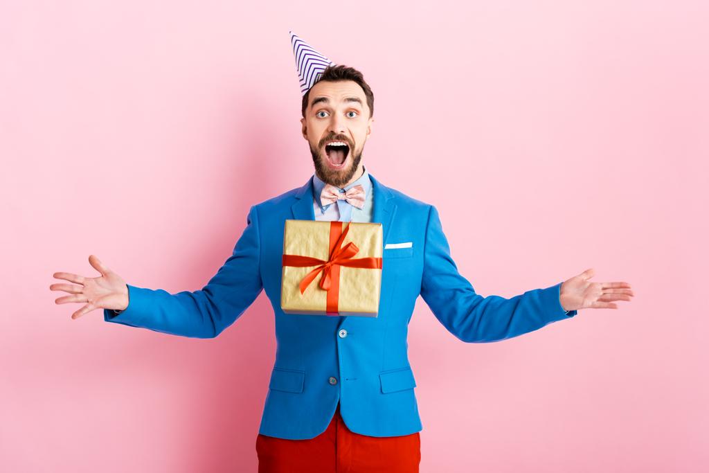 glücklicher Geschäftsmann in Partymütze wirft in der Luft Geschenk auf rosa  - Foto, Bild