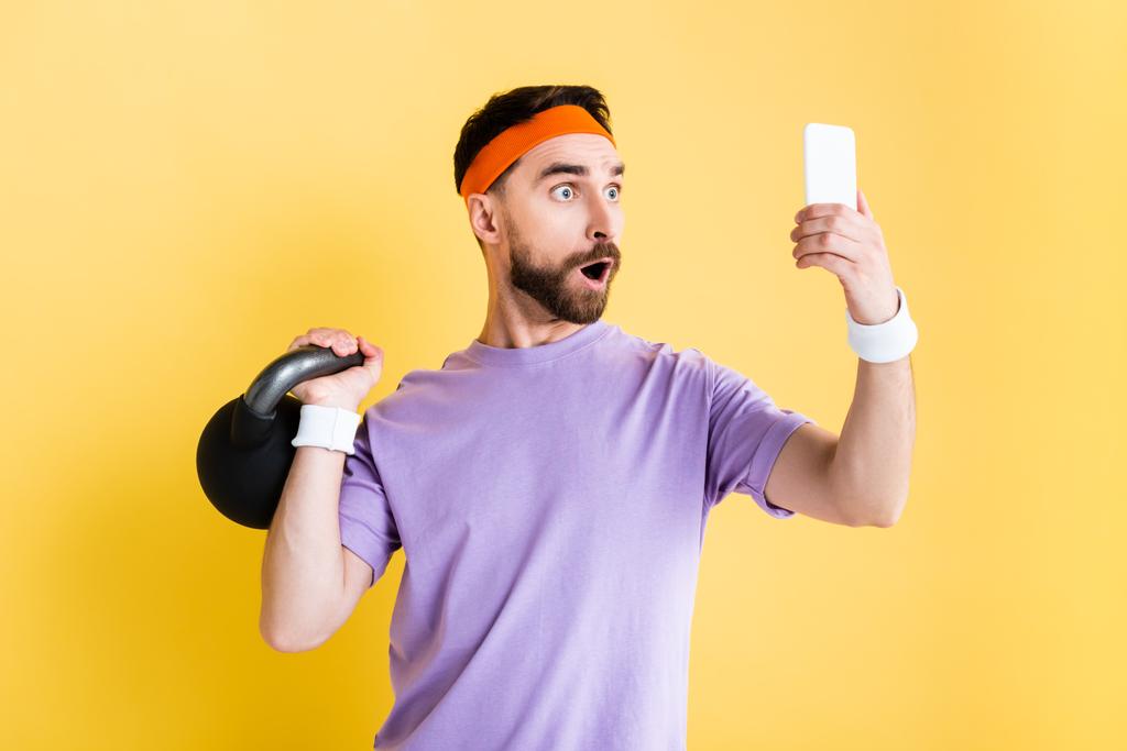 deportista sorprendido haciendo ejercicio con pesadas mancuerna y tomando selfie aislado en amarillo
 - Foto, Imagen