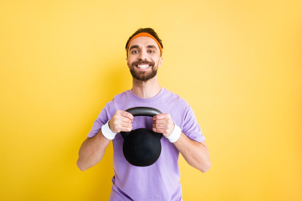 cheerful bearded sportsman exercising with heavy dumbbell isolated on yellow - Photo, Image