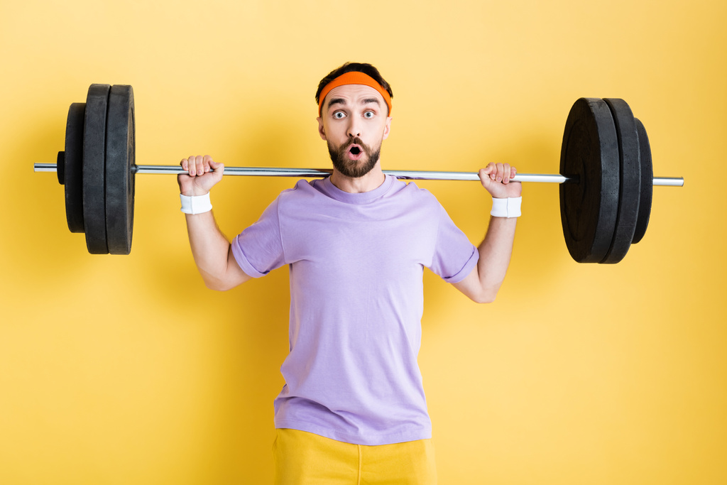 шокированный спортсмен, тренирующийся со штангой на желтом
 - Фото, изображение