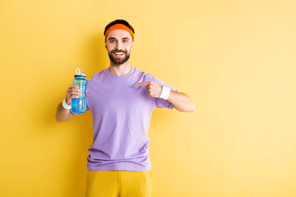 бородатый спортсмен указывает пальцем на спортивную бутылку на желтом
 - Фото, изображение