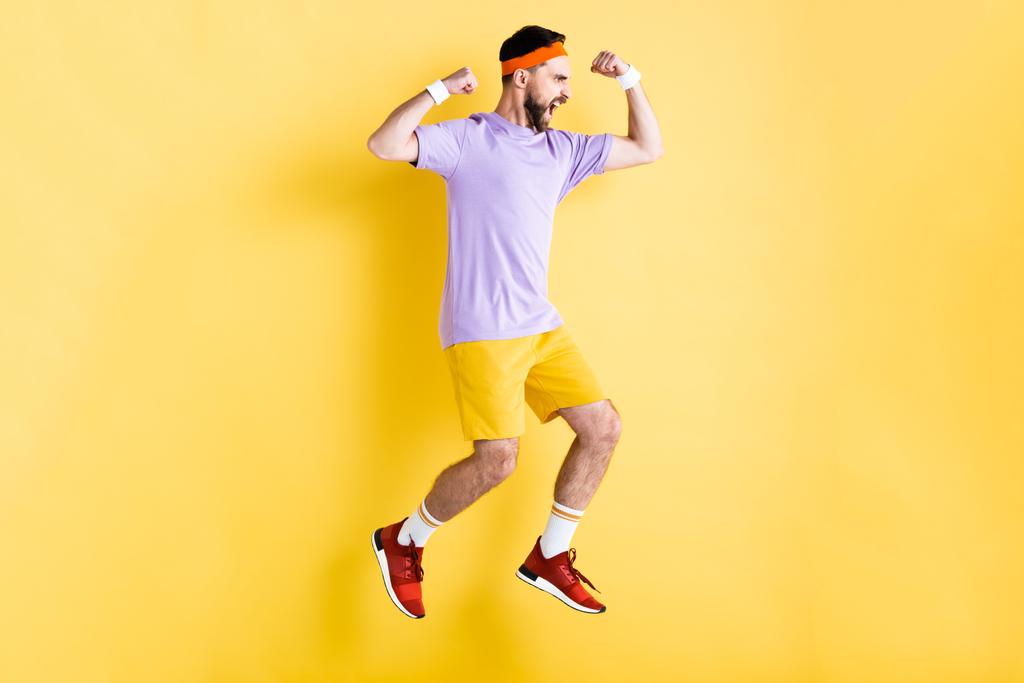 vista lateral del deportista barbudo excitado saltando sobre amarillo
 - Foto, imagen