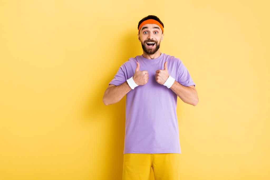 desportista barbudo alegre mostrando polegares para cima no amarelo
 - Foto, Imagem